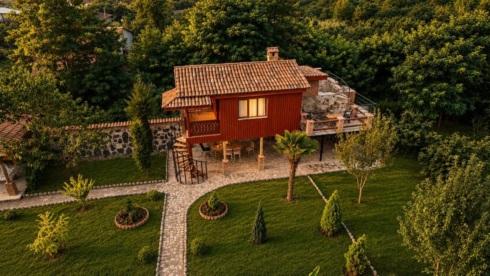ხის კოტეჯი ბოძებზე, ქვაფენილის ბილიკი და მოვლილი ბაღი ზემოდან